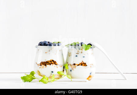 Le yogourt et granola avoine avec de la confiture, des bleuets et des feuilles de menthe dans un bocal en verre sur fond blanc, selective focus Banque D'Images