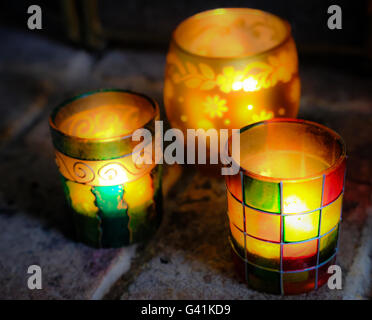 Foyer peu profond trio de pots de bougie en verre coloré vu avec des lampes de thé dans eux, placé devant un vieux feu de briques. Banque D'Images