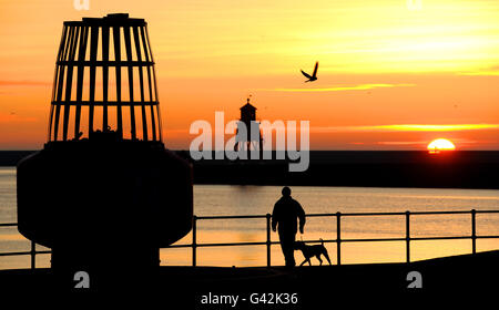 Un homme marche un chien tandis que le soleil se lève à Fish Quay près de l'embouchure de la rivière Tyne, North Shields. Banque D'Images