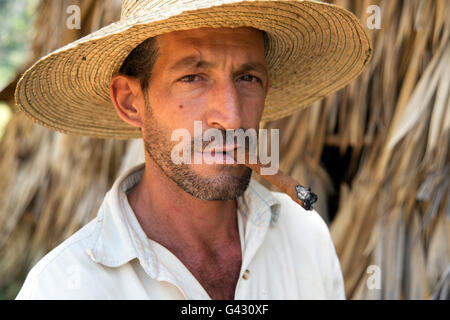 Portrait d'un agriculteur portant un chapeau de paille fumer un cigare avec le séchage du tabac de chaume maison dans l'arrière-plan Cuba Vinales Banque D'Images