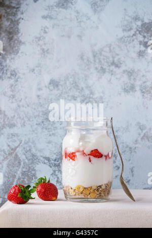 Petit-déjeuner sain du muesli, des fraises et du yogourt en pot Mason de verre avec une cuillère. Yaourt servi sur nappe textile blanc avec Banque D'Images