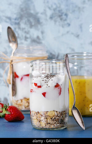 Petit-déjeuner sain muesli, yaourt et fraises à la mangue smoothie dans verre bocaux Mason. Servi sur table en bois bleu avec texte Banque D'Images