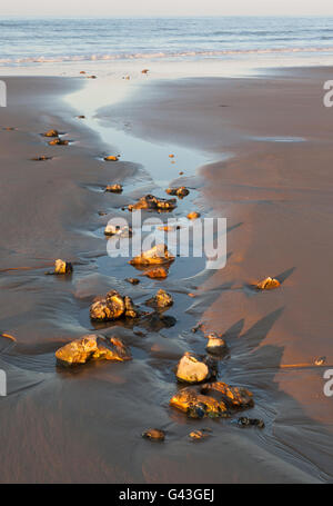 Une entrée d'eau de la mer parsemée de rochers sur une plage de sable. UK Banque D'Images
