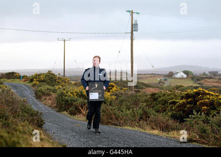 Garda Martin Reilly d'Achill arrive avec la boîte à balot au bureau de vote de Scoil Mhuire sur Inishbiggle (Inis Bigil en irlandais), une petite île habitée au large de la côte du comté de Mayo en Irlande, comme le vote commence à l'élection générale irlandaise 2011. Son nom en irlandais signifie 'île de jeûne et a seulement 24 électeurs inscrits. Banque D'Images