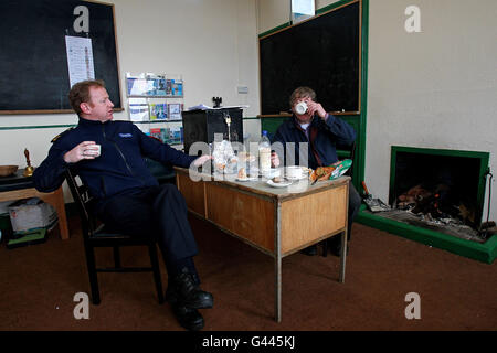 Garda Martin Reilly, d'Achill, discute avec l'officier présidant Micheal Leneghan sur le thé et les sandwiches dans le bureau de vote de Scoil Mhuire sur Inishbiggle (Inis Bigil en irlandais), une petite île habitée au large de la côte du comté de Mayo en Irlande, comme commence le vote à l'élection générale irlandaise 2011.Son nom en irlandais signifie 'île de jeûne et a seulement 24 électeurs inscrits. Banque D'Images