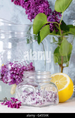 Pot en verre de fleurs lilas en sucre, verre et carafe d'eau avec du citron, lilas et branche de lilas blanc frais sur le linge de table Banque D'Images