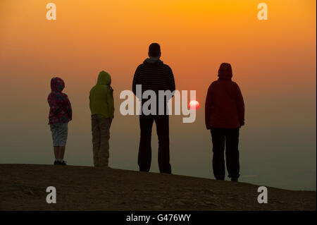 Une famille regardant le coucher du soleil sur le sommet de la colline Wrekin, Shropshire, Angleterre. Banque D'Images