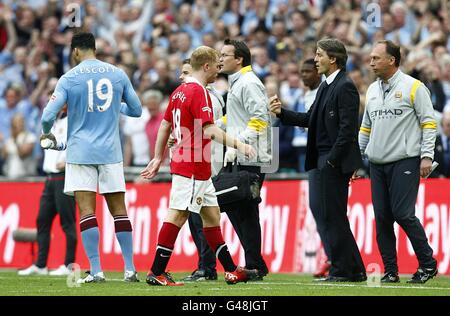 Paul Scholes de Manchester United (à gauche) laisse le terrain abattu après Être envoyé comme directeur de Manchester City Roberto Mancini (à droite) donne des instructions à ses joueurs Banque D'Images