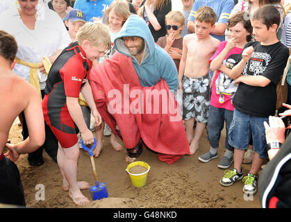 Michael Sheen sur la plage de Port Talbot aide un garçon avec son château de sable tout en jouant dans une pièce unique appelée « la passion » qui a commencé aujourd'hui et se poursuivra jusqu'à dimanche soir. Banque D'Images