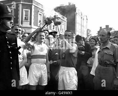 Frank Ede, à gauche, prend le flambeau olympique d'Austin Playford, avec le maire de Guildford, Alderman Arthur Williams, en train de regarder la cérémonie. Des foules de gens ont bordés les rues de Guildford pour voir la torche olympique être remise d'un relais à un autre, pour accélérer la torche sur son voyage à Wembley pour l'ouverture des Jeux Olympiques par le Roi. Banque D'Images