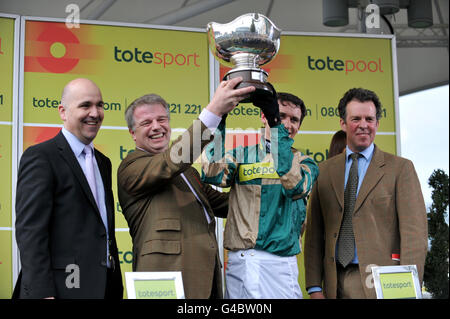 Le parti gagnant, dont le propriétaire Simon Clarke (deuxième à gauche), le jockey Paddy Brennan (deuxième à droite) et l'entraîneur Tom George (droite), lève le trophée après que Nacarat gagne le totesport Bowl Steeple Chase Banque D'Images