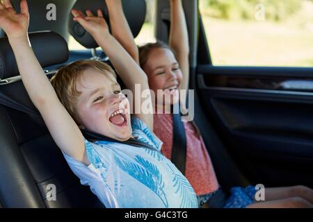 Parution du modèle. Frère et soeur dans le siège arrière de la voiture avec bras levés. Banque D'Images