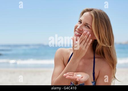 Parution du modèle. Jeune femme l'application de la crème solaire sur la plage. Banque D'Images