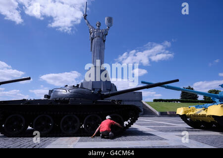 Un ouvrier d'entretien ukrainien lubrifie un char russe T-64 avec la statue de Rodina Mat Motherland en arrière-plan dans le complexe du Musée national de l'histoire de l'Ukraine dans la deuxième Guerre mondiale également appelé le Musée d'Etat ukrainien de la Grande Guerre patriotique situé dans la périphérie de la District de Pechersk à Kiev, la capitale de l'Ukraine Banque D'Images