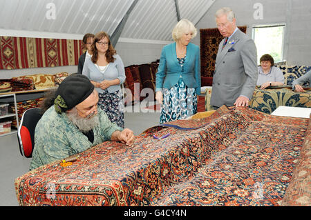 Le prince de Galles et la duchesse de Cornwall regardent Phil Beales, directeur de l'atelier, qui travaille sur un tapis Farahan de la fin du XIXe siècle de Chequers à David Bamford Carpets à Presteigne, Powys. Banque D'Images