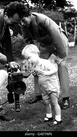 PA News 12/6/84 Romper adapté le Prince William, qui aura deux ans le 21 juin, s'intéresse à l'appareil photo d'un cameraman de MII dans le jardin de Kensington Palace, Londres, tandis que le père du jeune royal Prince Charles regarde sur. Banque D'Images