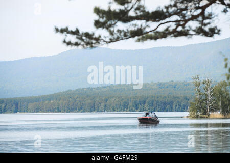 Motor Yacht flotte sur l'eau du lac entouré de montagnes et forêts Banque D'Images