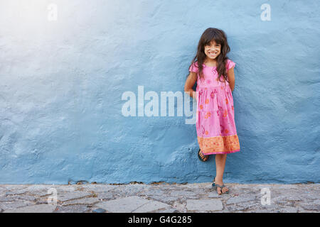 Full Length portrait of cute little girl smiling while standing against blue wall with copy space Banque D'Images