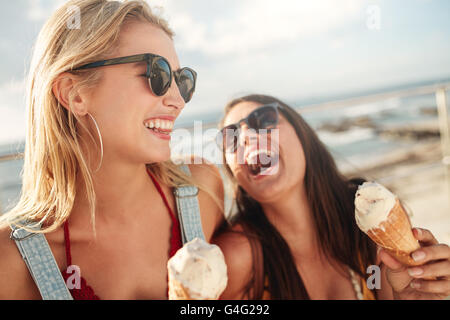 Deux jeunes femmes se tenant ensemble de rire et de manger de la crème glacée. Happy young female friends avec icecream profiter ensemble sur un Banque D'Images