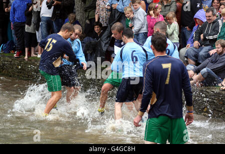 Bourton Rovers 1st XI (bleu clair) bataille pour possession avec Bourton Rovers 2nd XI (bleu foncé) lors du match annuel football dans la rivière à Bourton-on-the-Water, Gloucestershire le lundi des fêtes de rive. Les équipes de joueurs locaux s'affrontent lors de l'événement annuel qui se déroule dans la rivière Windrush, au centre de la ville. Banque D'Images