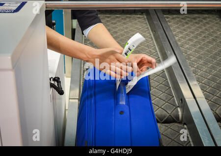 Check-in employé attache une étiquette à bagages valise de passager - close up of hands Banque D'Images