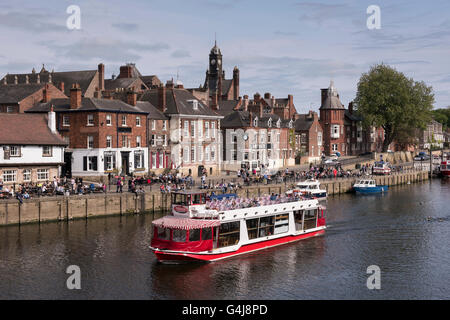 City Cruises bateau naviguant sur la rivière pittoresque ensoleillée Ouse, devant les gens se détendant à l'extérieur des pubs et restaurants au bord de la rivière - York, Yorkshire, Angleterre, Royaume-Uni. Banque D'Images