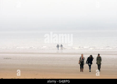 Les membres du public portant des vêtements plus semblables à la météo automnale habituelle, marchez sur une plage humide et venteuse à St Andrews, en Écosse, en contraste avec celle du ciel bleu clair et du temps chaud dans le sud du Royaume-Uni, La vague de chaleur va se poursuivre la semaine prochaine dans certaines régions de Grande-Bretagne, après un week-end de températures record. Banque D'Images