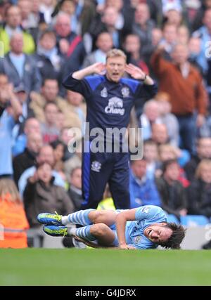 David Silva de Manchester City est blessé sur le sol suivant Un défi par Jack Rodwell d'Everton et le directeur David Moyes (derrière) réagit sur la ligne de contact Banque D'Images