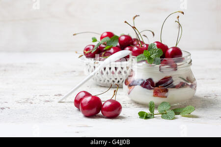 Régime d'été le petit déjeuner. Le yaourt avec de cerises fraîches, menthe dans un bocal en verre sur un fond de bois blanc Banque D'Images