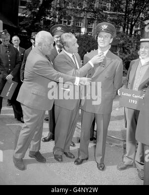 L'un des nouveaux uniformes proposés pour les postiers britanniques est vu par le ministre des postes, M. Ernest Marples (au centre) et M. Langley Powe, dont la firme l'a conçu, à St Martin-le-Grand, Londres. L'uniforme, en matériau gris et croisé, est porté par le modèle Simon Hill. Banque D'Images