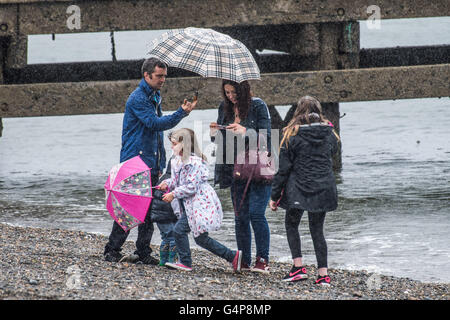 Aberystwyth, Pays de Galles, Royaume-Uni. 19 Juin, 2016. Météo France : une famille s'abritant sous leurs parasols à la station balnéaire d'Aberystwyth par temps humide et froid dimanche après-midi à la mi-juin. Comme le jour le plus long de l'année - le solstice d'été - approches, une bande de forte pluie déferle en provenance de l'ouest, ce qui porte le temps anormalement froid et couvert pour la plupart du Royaume-Uni dans les prochains jours de crédit : Keith morris/Alamy Live News Banque D'Images