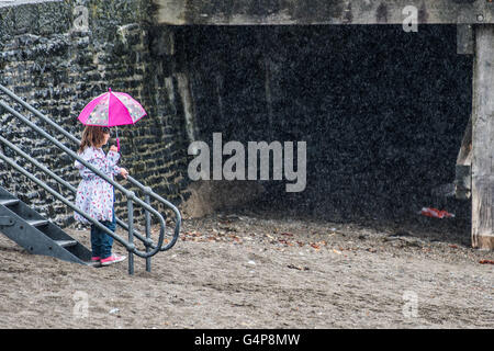 Aberystwyth, Pays de Galles, Royaume-Uni. 19 Juin, 2016. Météo France : une jeune fille enfant protège sous son parapluie rose à la station balnéaire d'Aberystwyth par temps humide et froid dimanche après-midi à la mi-juin. Comme le jour le plus long de l'année - le solstice d'été - approches, une bande de forte pluie déferle en provenance de l'ouest, ce qui porte le temps anormalement froid et couvert pour la plupart du Royaume-Uni dans les prochains jours de crédit : Keith morris/Alamy Live News Banque D'Images