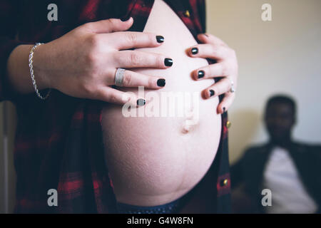 Une femme enceinte tient sa bosse de bébé. Père-à-être est assis dans l'arrière-plan; expectant parents. Banque D'Images
