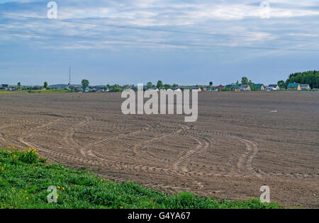 Champ labouré brun agricole et le village derrière le terrain. Banque D'Images