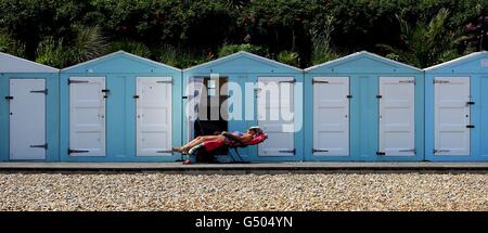 Une femme aime le soleil à l'extérieur de sa cabane de plage à Eastbourne, East Sussex. Banque D'Images