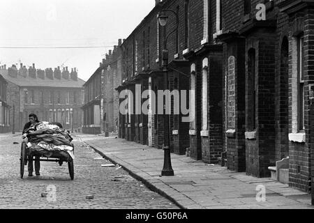 Un Rag and Bone Man pousse son chariot dans une rue pavée, passant devant des maisons à boarboared-up, à Lower Broughton, Salford, une région autrefois décrite dans un livre comme un « bidonville classique », mais où environ mille familles vivent encore. Banque D'Images