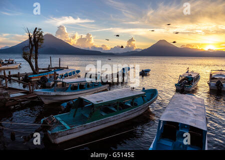 Des oiseaux volent par Taxis amarré à quai à Panajachel comme le coucher de soleil sur les volcans du Lago de Atitlan au Guatemala Banque D'Images