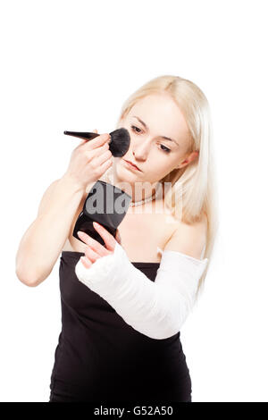 Fille blonde avec un bras cassé dans le plâtre de la difficulté à mettre un rouge à lèvres Banque D'Images
