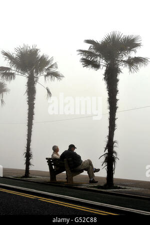 Un couple s'assoit sur un banc de front de mer protégé par un brouillard, en attendant la vague de chaleur prévue le week-end pour atteindre Southend-on-Sea, Essex. Banque D'Images