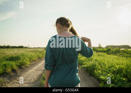 Teen girl walking away on rural road entre les champs Banque D'Images