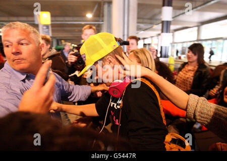 Justin Bieber (casquette jaune) est pris par les fans alors qu'il arrive au terminal 5 de l'aéroport d'Heathrow avant le lancement de son album. Banque D'Images