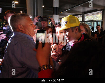 Justin Bieber (casquette jaune) est pris par les fans alors qu'il arrive au terminal 5 de l'aéroport d'Heathrow avant le lancement de son album. Banque D'Images