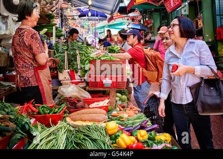 Un nouveau client et sa branche d'aider à discuter avec le propriétaire d'un kiosque de légumes sur Graham Street, Central, Hong Kong. Banque D'Images