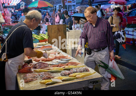 Un nouveau client les demandes de renseignements sur le prix d'un peu de poisson à l'étal d'un vendeur de poisson sur Chun Yeung Street Market à Northpoint, Hong Kong. Banque D'Images