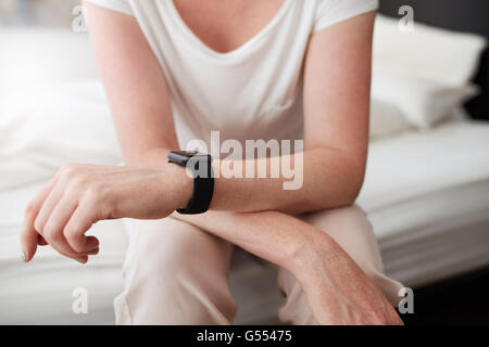 Cropped shot of a woman sitting on bed porter une montre-bracelet, elle est dans la chambre à la maison. Se concentrer sur les mains des femmes et montre-bracelet. Banque D'Images