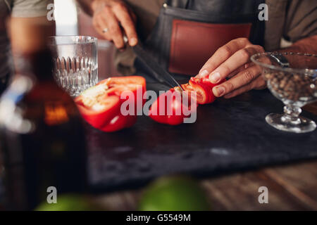 Gros plan des mains barman chopping poivron rouge sur la planche à découper. Expérimenter de nouvelles idées de cocktails. Banque D'Images