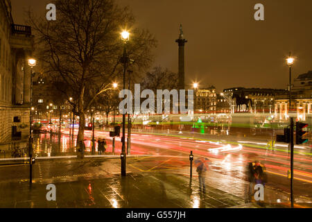 Londres, Angleterre, Trafalgar Square la nuit sous la pluie avec des bus à double étage, les gens avec des parasols Banque D'Images