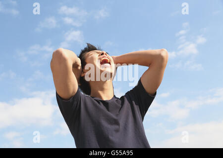 Jeune homme japonais cheering contre le ciel bleu Banque D'Images