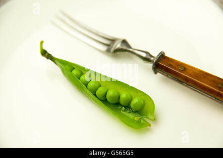 Gousse de pois verts et la fourche sur la plaque blanche. Banque D'Images