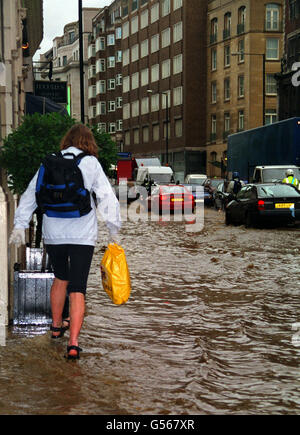 Une femme traverse une rue inondée à Knightsbridge, Londres, après une pluie torrentielle pendant la nuit.Les navetteurs ont dû faire face au chaos quand les arbres ont été abattus par les vents violents qui ont bloqué les voies ferrées et les routes.*les experts du climat ont déclaré que les tempêtes qui ont balayé le sud du pays de Galles et l'Angleterre pendant la nuit étaient parmi les pires au cours des dernières années.Jusqu'à 80 mm de pluie sont tombés en 24 heures et des vitesses de vent allant jusqu'à 90 mph ont été signalées. Banque D'Images